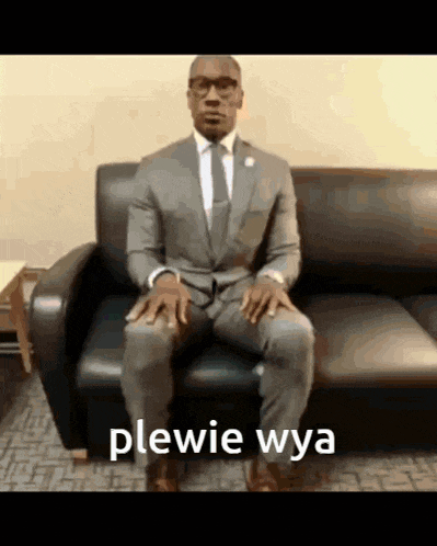 a man in a suit and tie is sitting on a couch with the word plewie wya written on the bottom