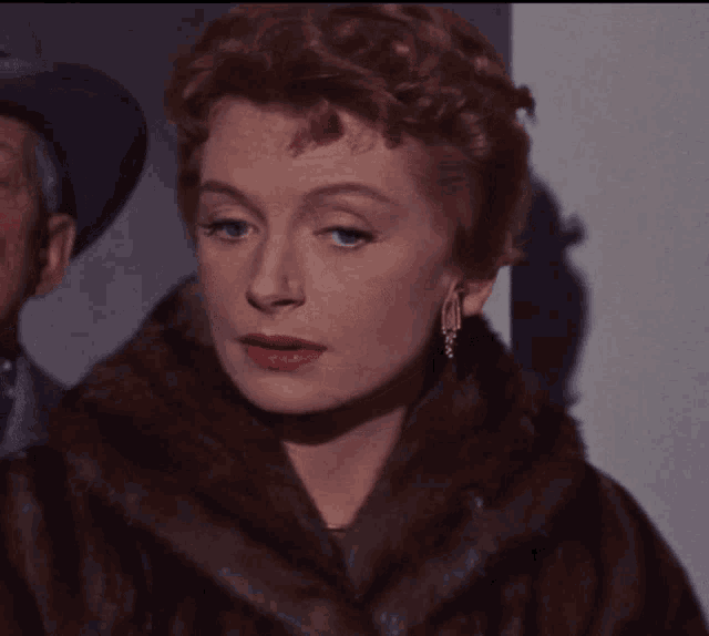 a woman with red hair wearing a fur coat and earrings looks at the camera