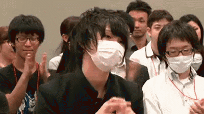 a man wearing a face mask is sitting in a crowd of people applauding .