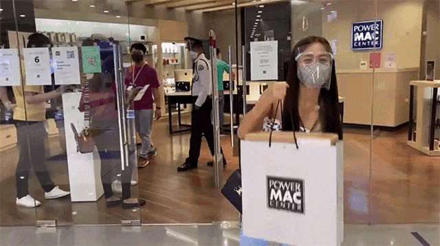 a woman wearing a mask is holding a bag in front of a power mac center