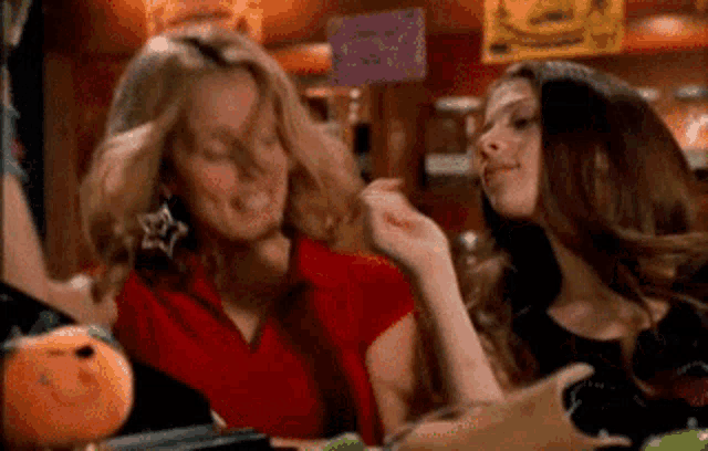 two women are sitting at a table with a pumpkin on the table .