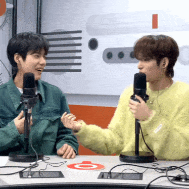 a man in a yellow sweater talks into a microphone next to another man