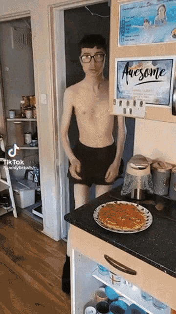 a shirtless man stands in front of a refrigerator that says awesome on it