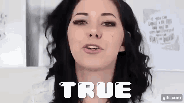 a woman with black hair is standing in front of a white wall and the word true is on the screen .