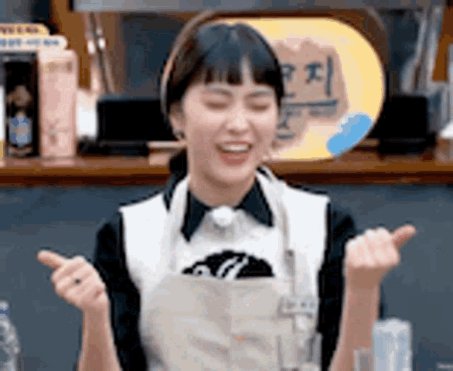 a woman wearing an apron is sitting at a table with her arms outstretched and smiling .