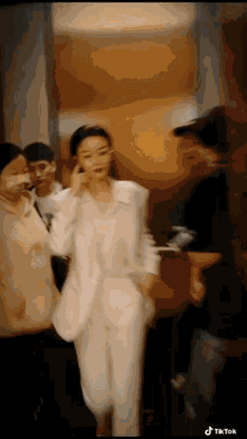 a woman in a white suit is walking down a hallway with people .