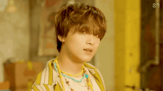 a young man wearing a striped shirt and necklaces looks at the camera