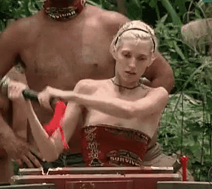 a woman is standing next to a man in the jungle holding a sword .