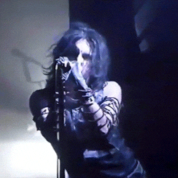 a woman with blue hair is singing into a microphone in a dark room