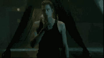 a man in a black tank top is standing in front of a woman 's legs in a dark room .