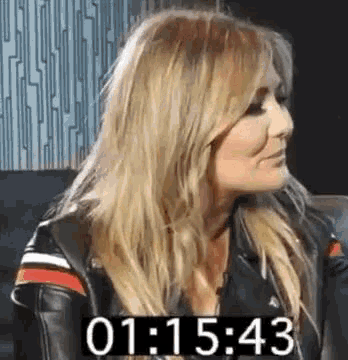 a woman in a leather jacket is sitting in front of a clock that shows the time as 1:43 .