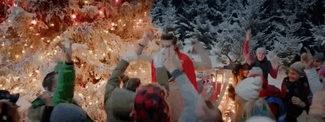 a group of people are dancing in front of a christmas tree in the snow .