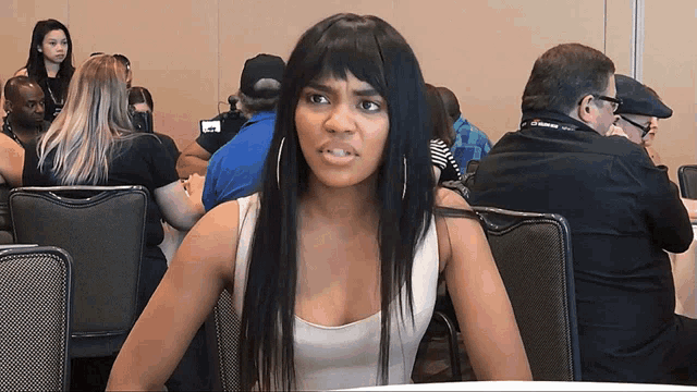 a woman in a white tank top sits in a crowded room with a man wearing a lanyard that says cbs