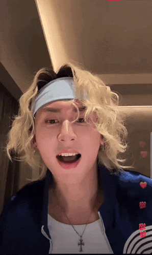 a man with blonde curly hair wearing a headband and a necklace