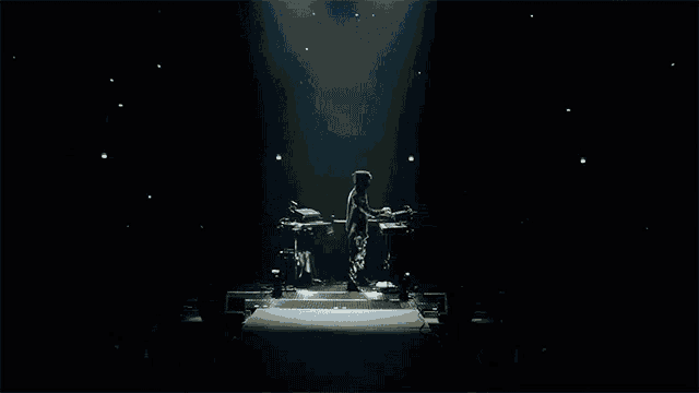 a man in a hooded jacket stands on a stage playing a keyboard