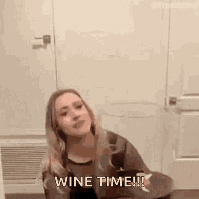 a woman is sitting at a table with a glass of wine and says `` wine time '' .