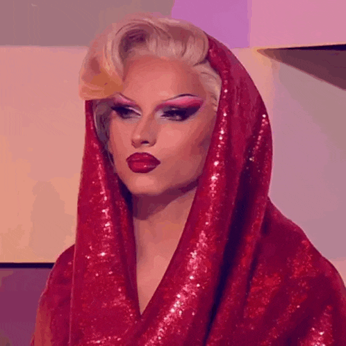 a drag queen is wearing a red sequined robe and a red head scarf .