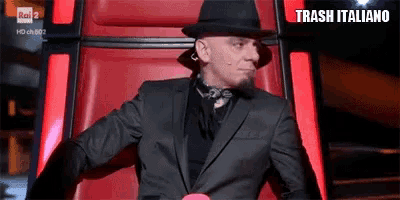 a man in a suit and hat is sitting in a red chair with the words trash italiano on the bottom