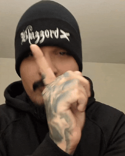 a man wearing a black beanie with the word faggord on it points his finger