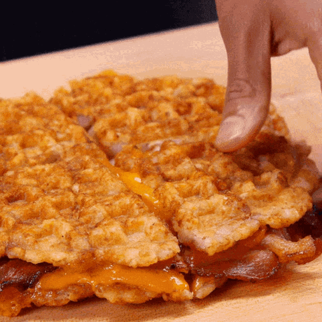 a close up of a person 's finger touching a waffle with cheese and bacon