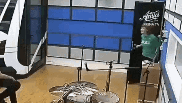 a man in a green shirt is playing drums in front of a sign that says amici