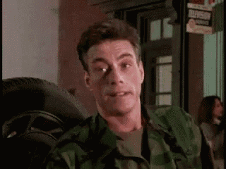 a man in a camouflage jacket is sitting in front of a tire and making a funny face .