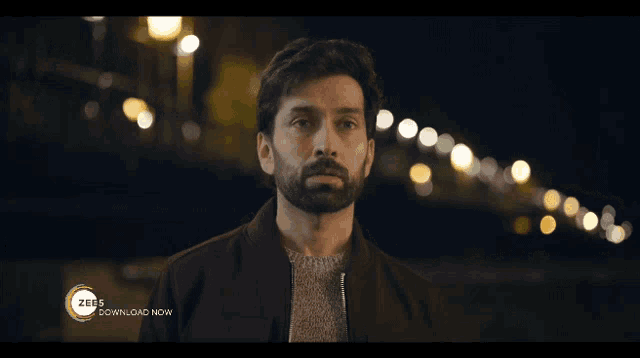 a man with a beard is standing in front of a sign that says zee download now