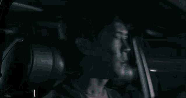 a man is sitting in a car at night with smoke coming out of the windshield