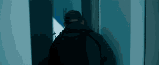 a man in a black jacket and hat is walking through a doorway