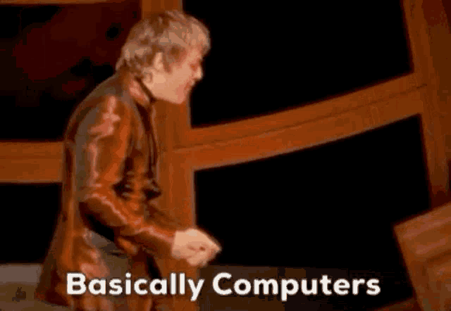 a man in a red suit is standing on a stage with the words basically computers written below him .