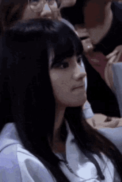 a girl with long black hair is sitting in a crowd of people .