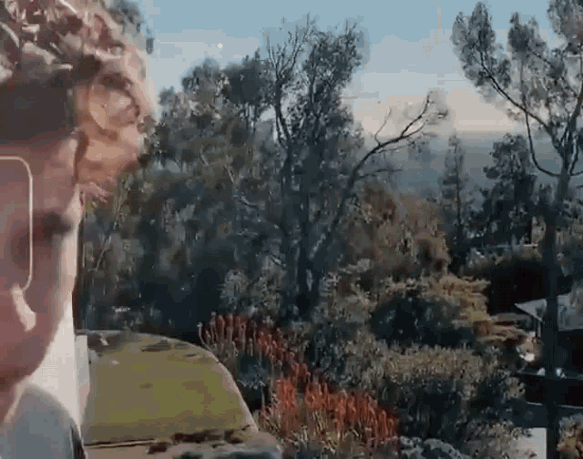 a man wearing sunglasses is looking out a window at trees and a house .