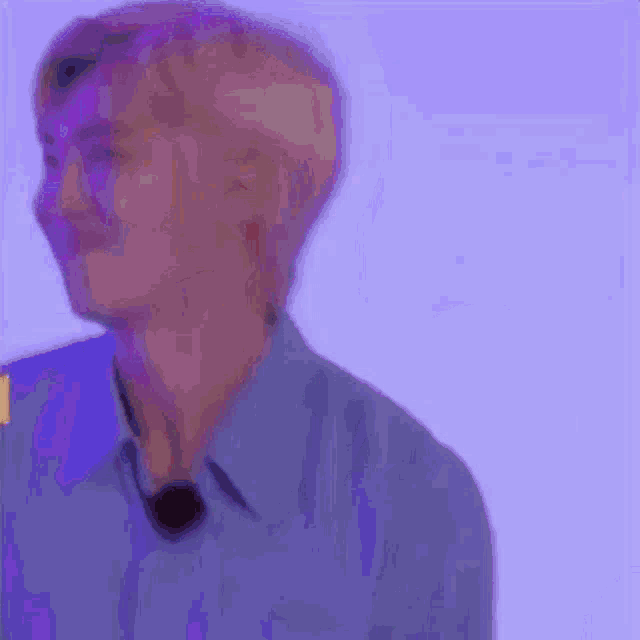 a man in a blue shirt is standing in front of a purple background and looking at the camera .
