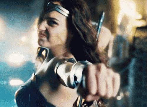 a woman in a wonder woman costume is holding a sword and pointing it at the camera .