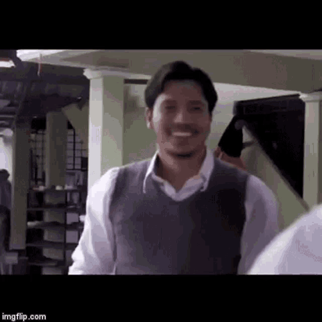 a man with a beard is smiling in a room while wearing a vest .