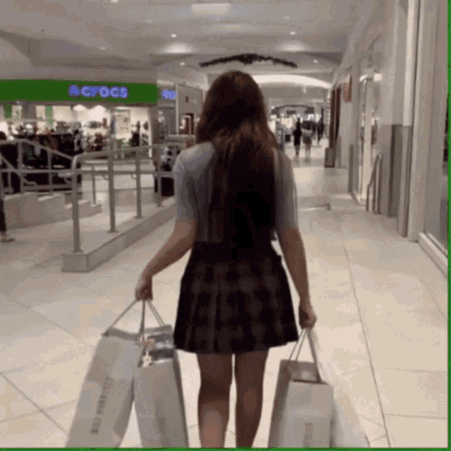 a woman is carrying shopping bags in a mall with a crocs store in the background