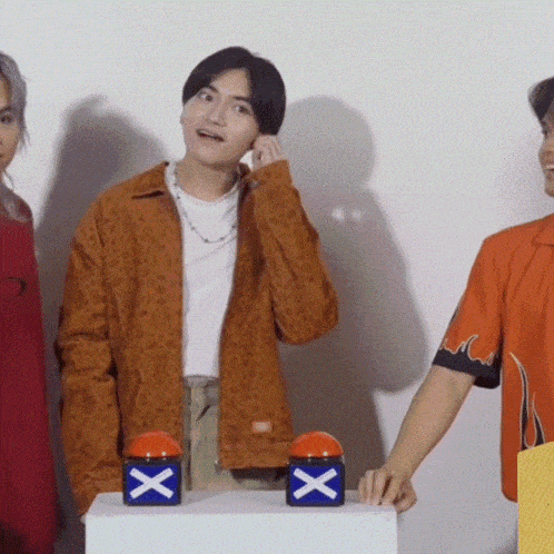 a man in an orange jacket is talking on a cell phone while standing next to two boxes with x on them