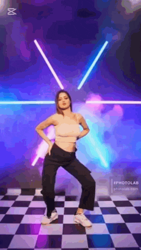 a woman is dancing on a checkered floor in front of a neon light .