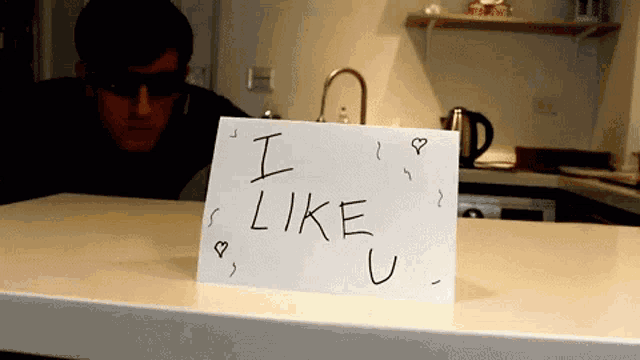 a man wearing sunglasses stands behind a card that says i like u