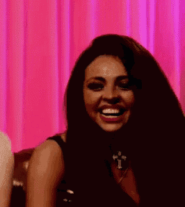 a woman is laughing in front of a pink curtain while wearing a choker necklace .