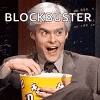 a man in a suit and tie is eating popcorn from a yellow bucket .
