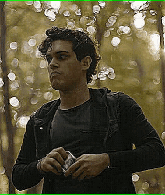 a man in a black jacket is holding a camera in front of a blurry background of trees