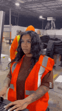 a woman in an orange vest is typing on a laptop