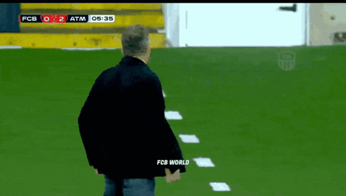 a man in a black jacket stands on a soccer field with fcb world written on his back