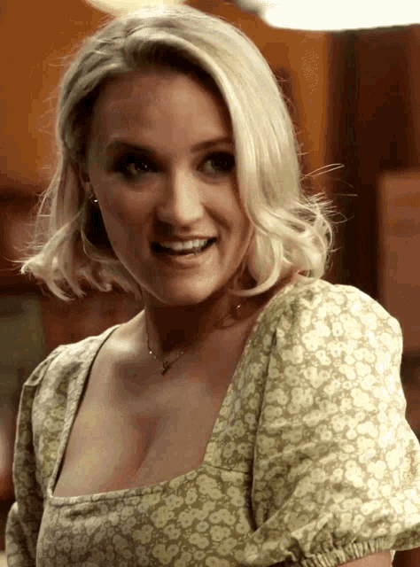 a blonde woman wearing a green floral top smiles