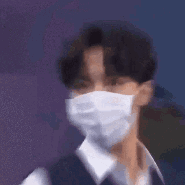 a young man wearing a white face mask is looking at the camera .