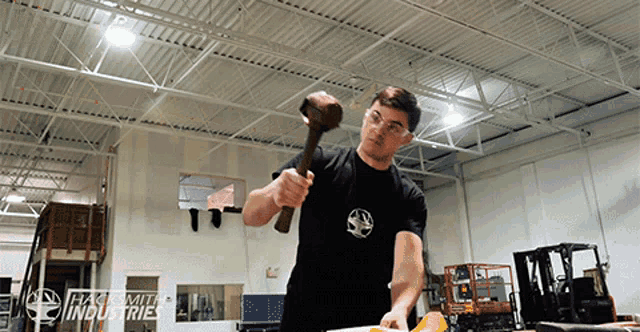 a man in a black shirt is holding a hammer in front of a sign that says " commit industries " on it