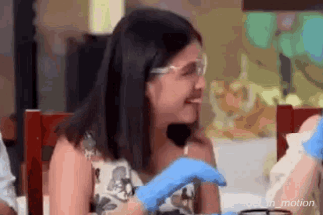 a woman wearing glasses and gloves is sitting at a table .