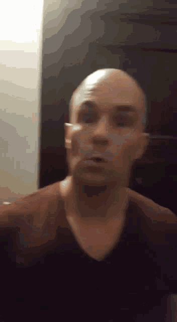 a man with a shaved head and a black shirt is making a funny face