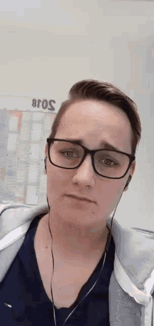 a woman wearing glasses and headphones is standing in front of a wall with the year 2018 on it .